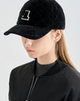Person wearing a black quilted cap with a logo on a light gray background