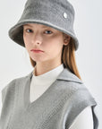 Person wearing a gray bucket hat and knitted vest on a white background
