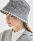 Person wearing a gray bucket hat with a button on a light gray background