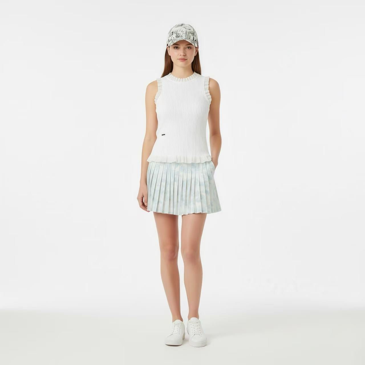 Woman wearing a white sleeveless top and pleated skirt with a cap on a white background
