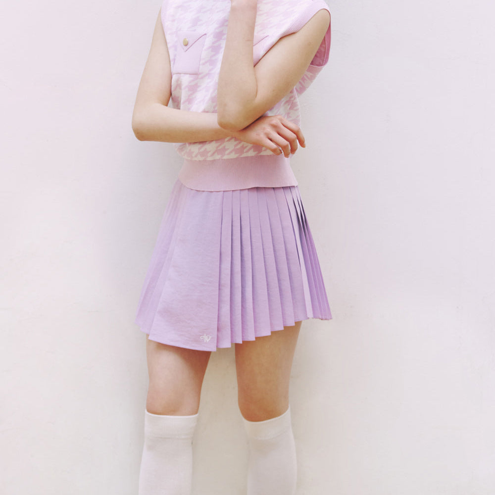 A model wearing a light purple pleated mini skirt and a matching light pink sleeveless top, paired with white knee-high socks, set against a plain light background.