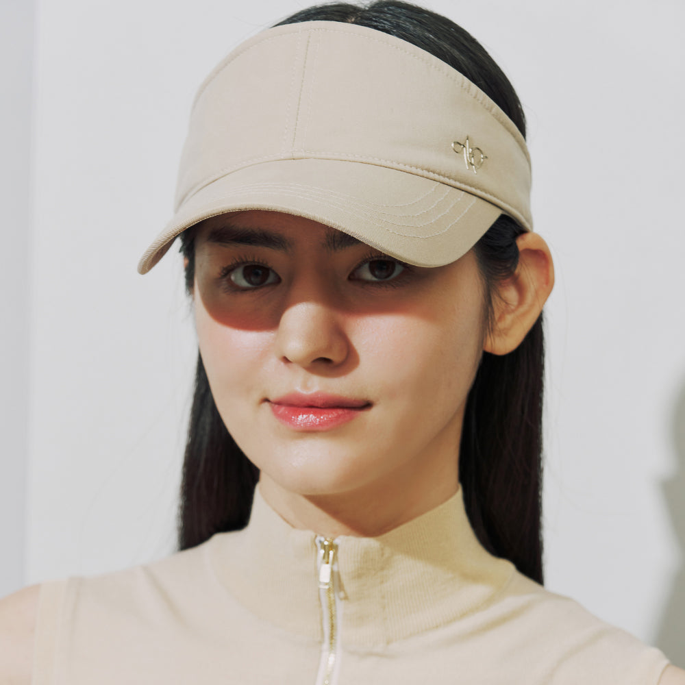 A woman wearing a beige visor cap with a small gold logo and a matching beige high-collar zip top, photographed against a clean light background.