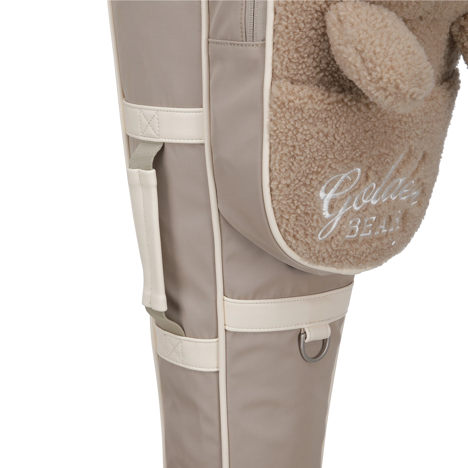 Close-up of a beige and cream padded bag with a plush brown teddy bear ear and pocket, featuring the embroidered text 'Golden Bear'.