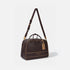 A dark brown leather duffel bag with tan accents, featuring a long shoulder strap, top handles, and the &