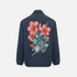 A navy blue jacket shown from the back, featuring a large graphic print of pink hibiscus flowers and green leaves on the upper back, with a white signature-style graphic overlay.