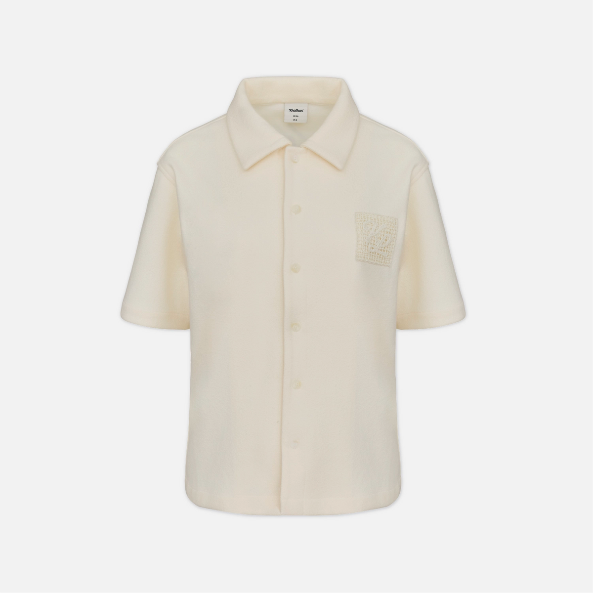 A short-sleeve cream-colored button-up shirt with a pointed collar and a textured square patch on the chest pocket, shown against a plain light gray background.