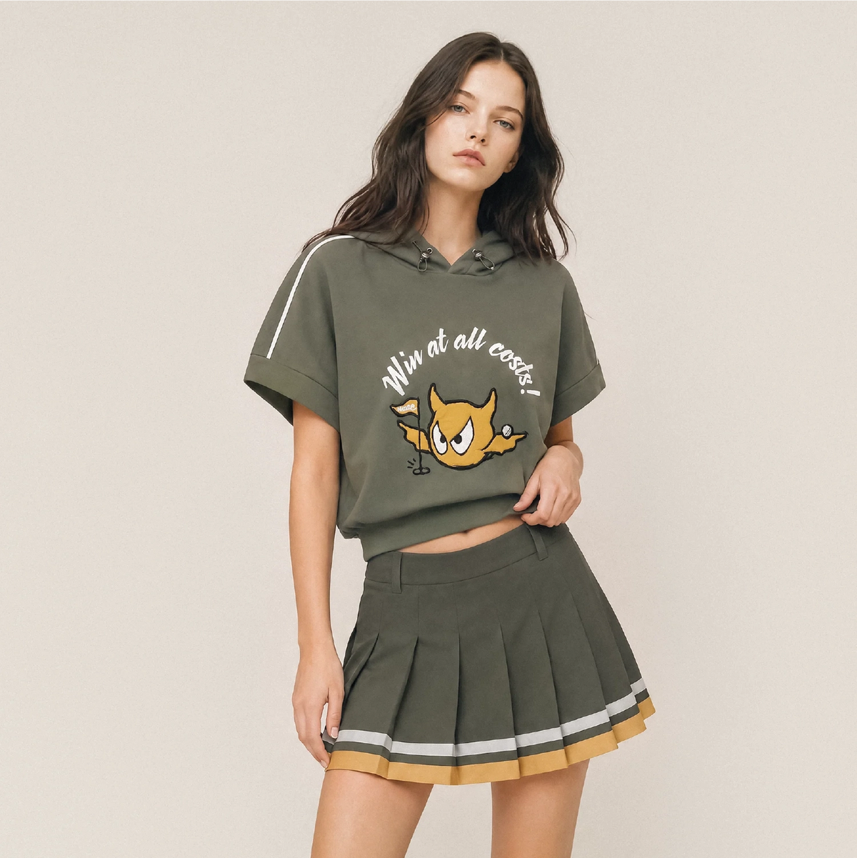 Model wearing khaki pleated golf skort with color tipped hem.