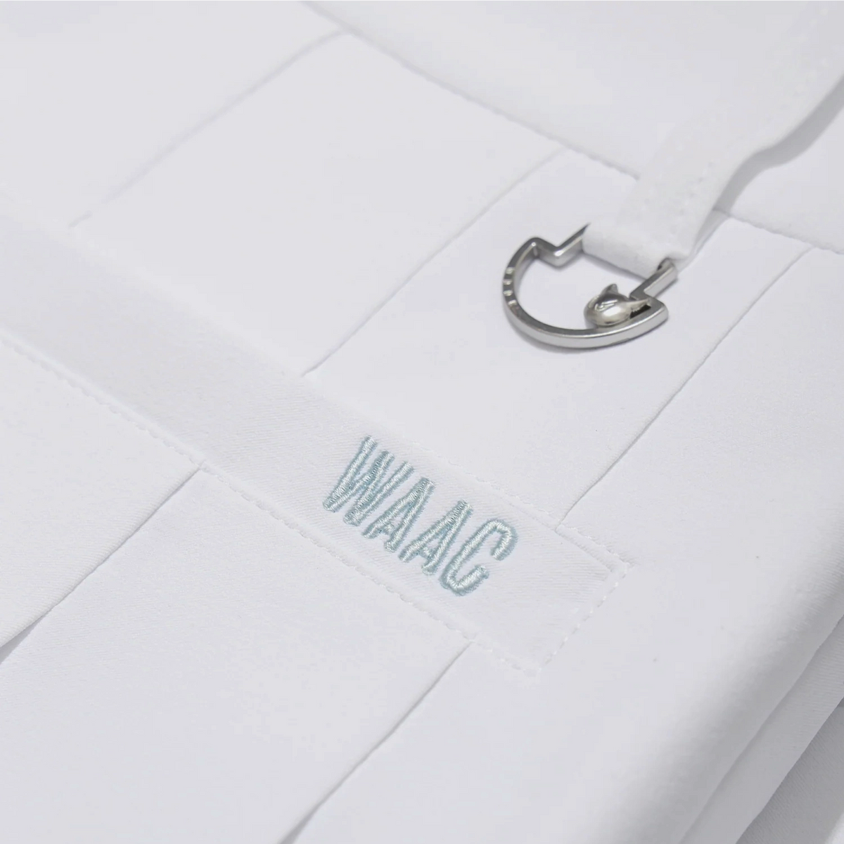 Close-up of white pleated golf skort with WAAC logo and metal ring