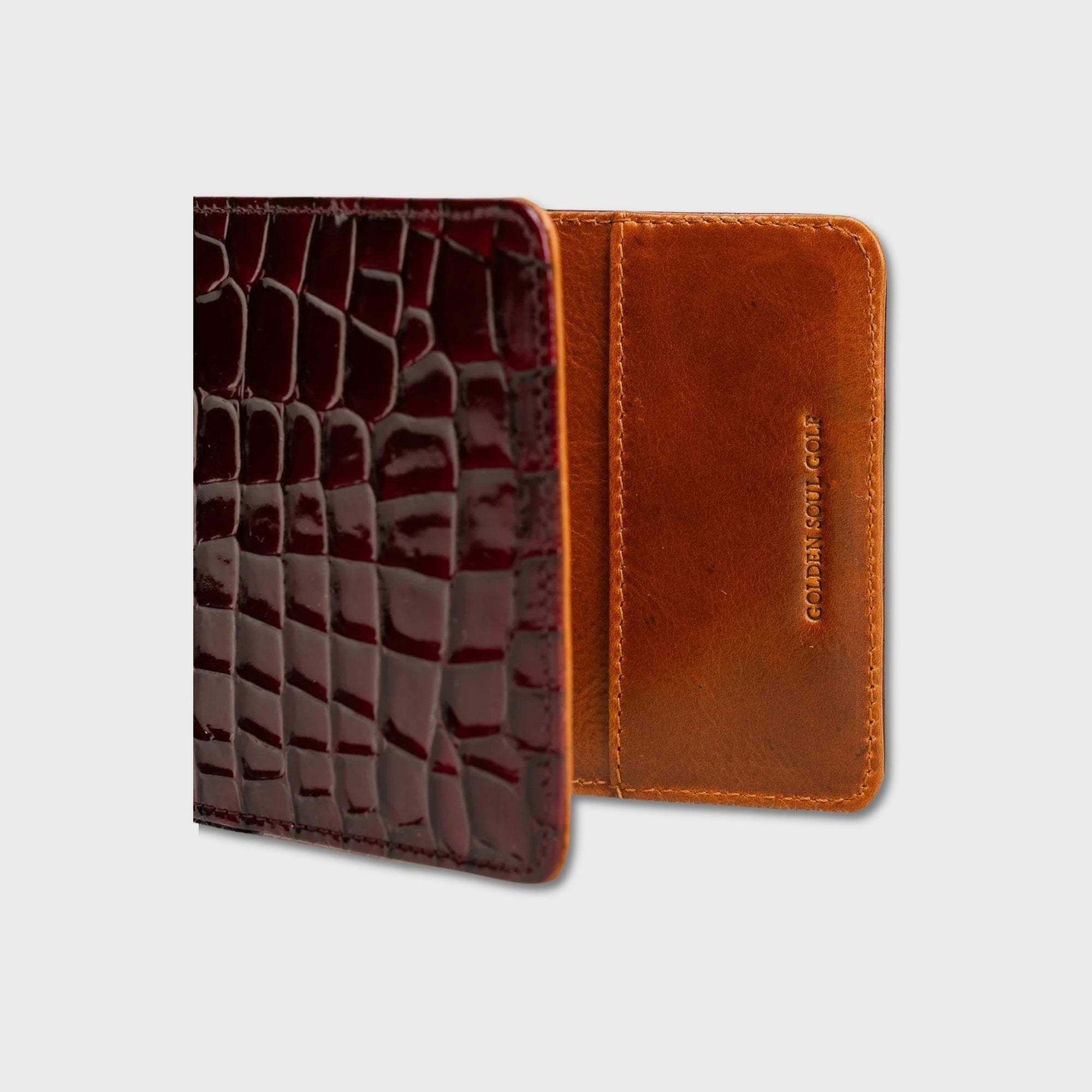 A two-tone leather yardage book holder shown open on a light gray background. The left side features a glossy dark burgundy crocodile-embossed texture, while the right side is a smooth warm brown leather with 'GOLDEN SOUL GOLF' debossed vertically.