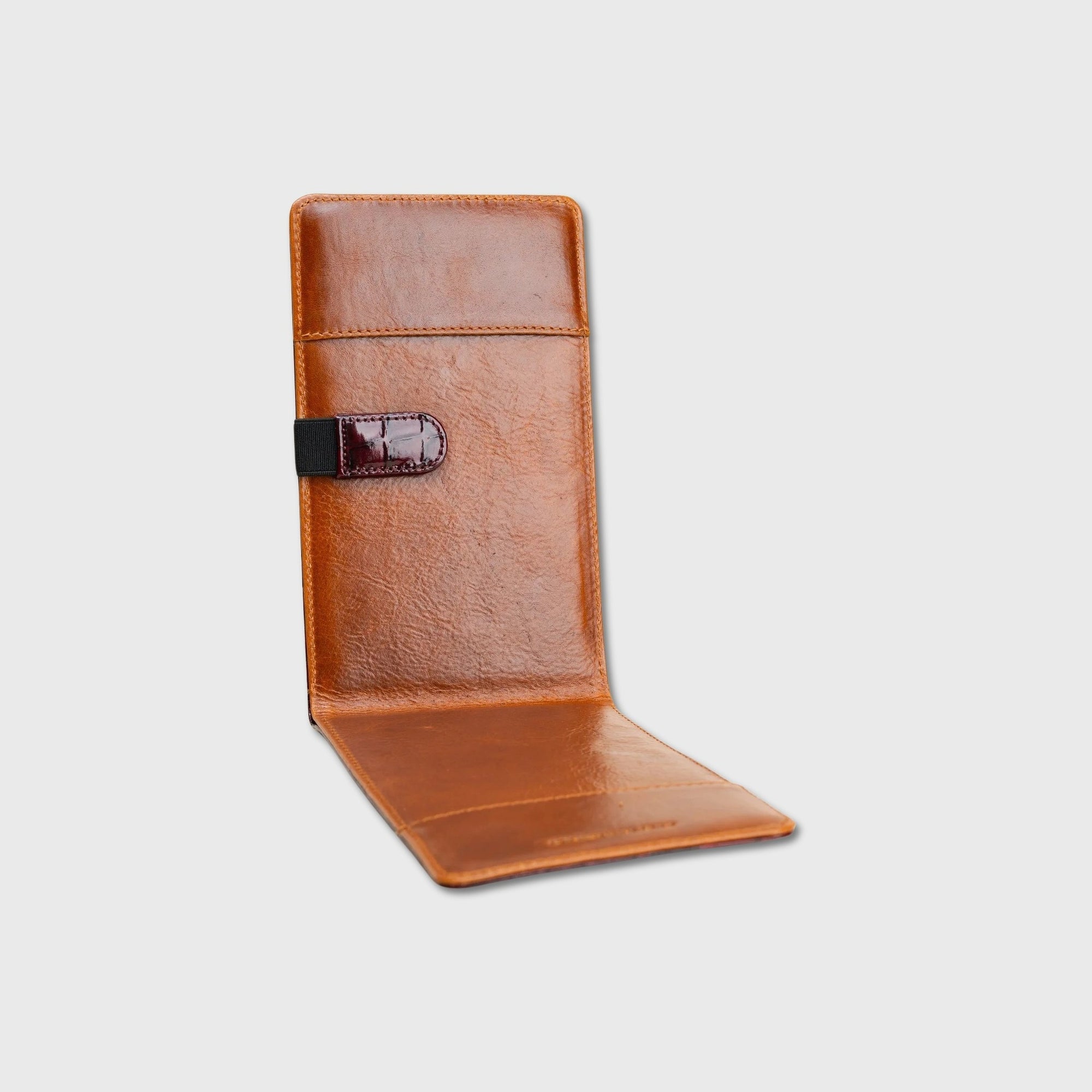 A tan leather yardage book holder shown open against a light gray background, featuring a black strap closure with a small brand patch.