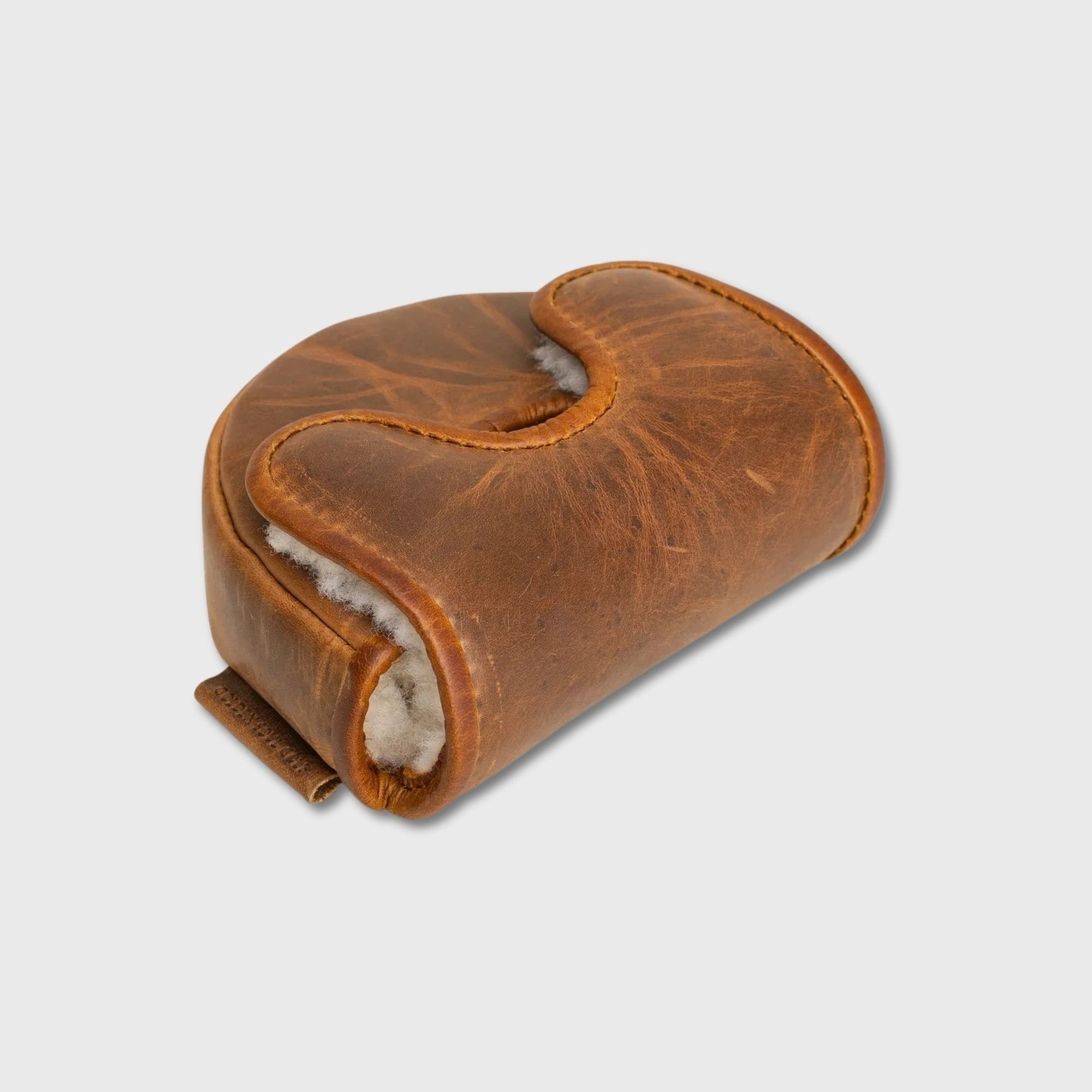 A brown leather OZ1 Putter Cover with a curved, saddle-like shape, featuring a white shearling or wool lining visible along the edges, set against a light gray background.