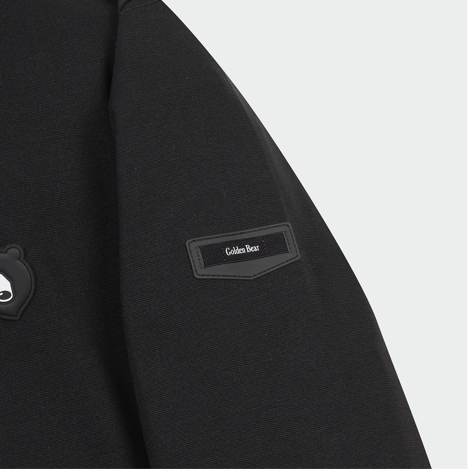 Close-up of a black sweatshirt sleeve featuring a dark gray shield-shaped patch with the text 'Golden Bear' and a small bear-head patch on the opposite shoulder.