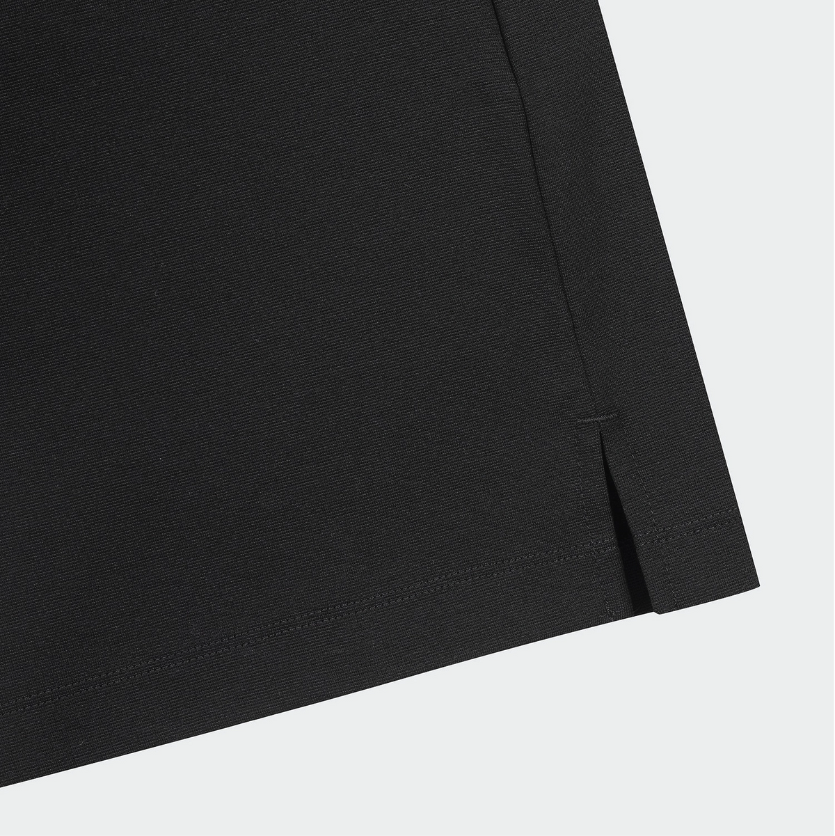 Close-up detail of a black garment corner showing a folded hem with a small side slit, on a light gray background.