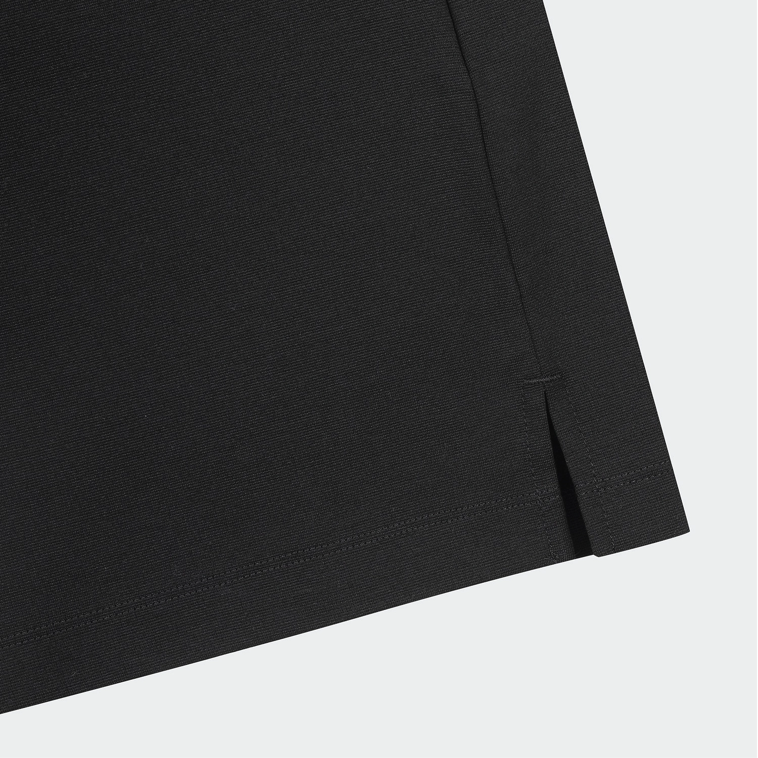 Close-up detail of a black garment corner showing a folded hem with a small side slit, on a light gray background.