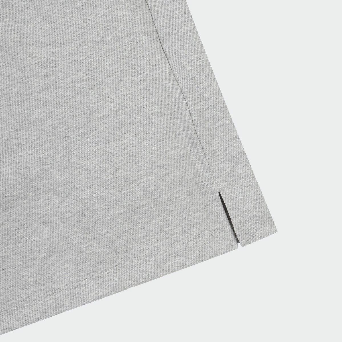 Close-up of a light gray heathered fabric corner with a visible seam and small slit detail, set against a plain light gray background.