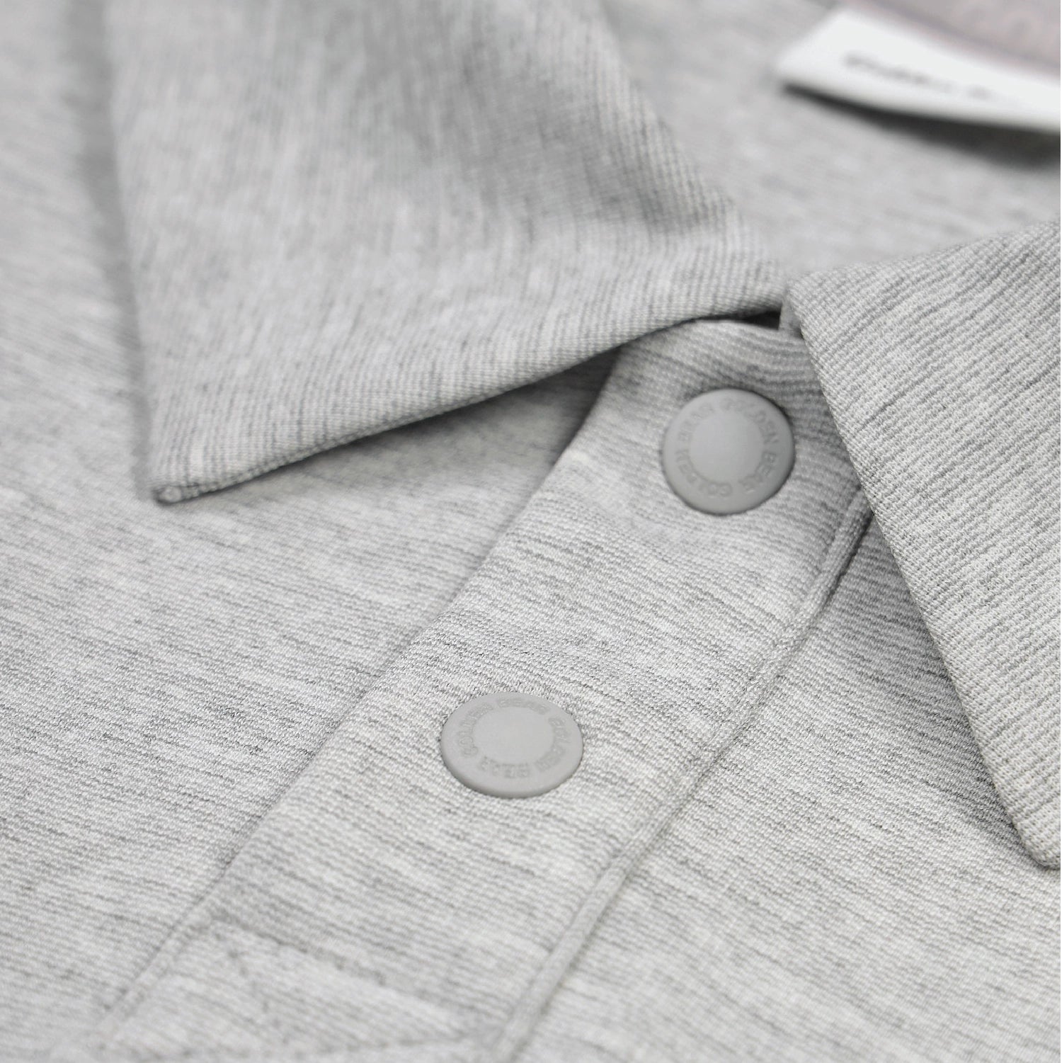 Close-up of a light gray heathered knit garment with a collar and two matching round snap buttons.