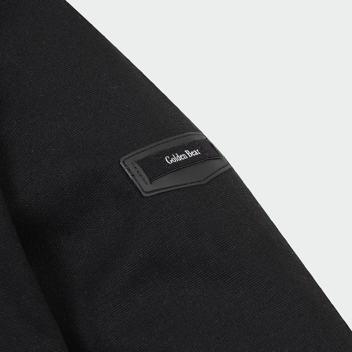 Close-up of a black textured garment sleeve with a black rectangular patch on the upper arm featuring the Golden Bear logo in white text.