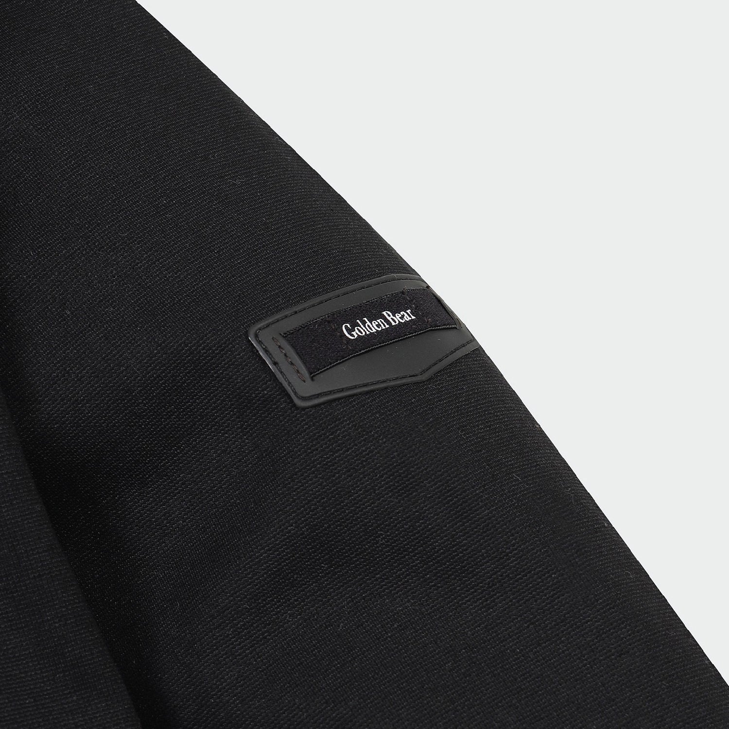 Close-up of a black textured garment sleeve with a black rectangular patch on the upper arm featuring the Golden Bear logo in white text.