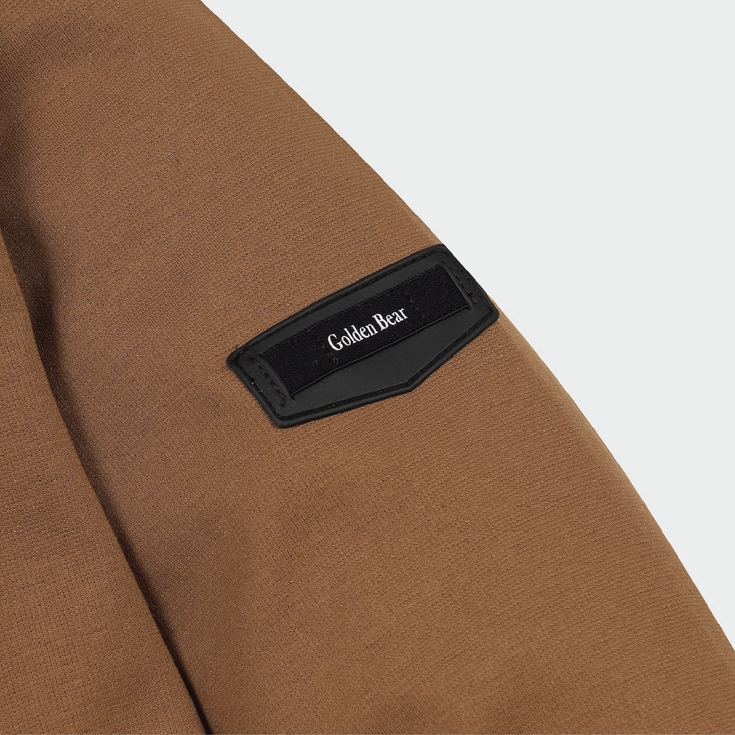 Close-up of a brown textured garment sleeve with a black embroidered patch reading Golden Bear.