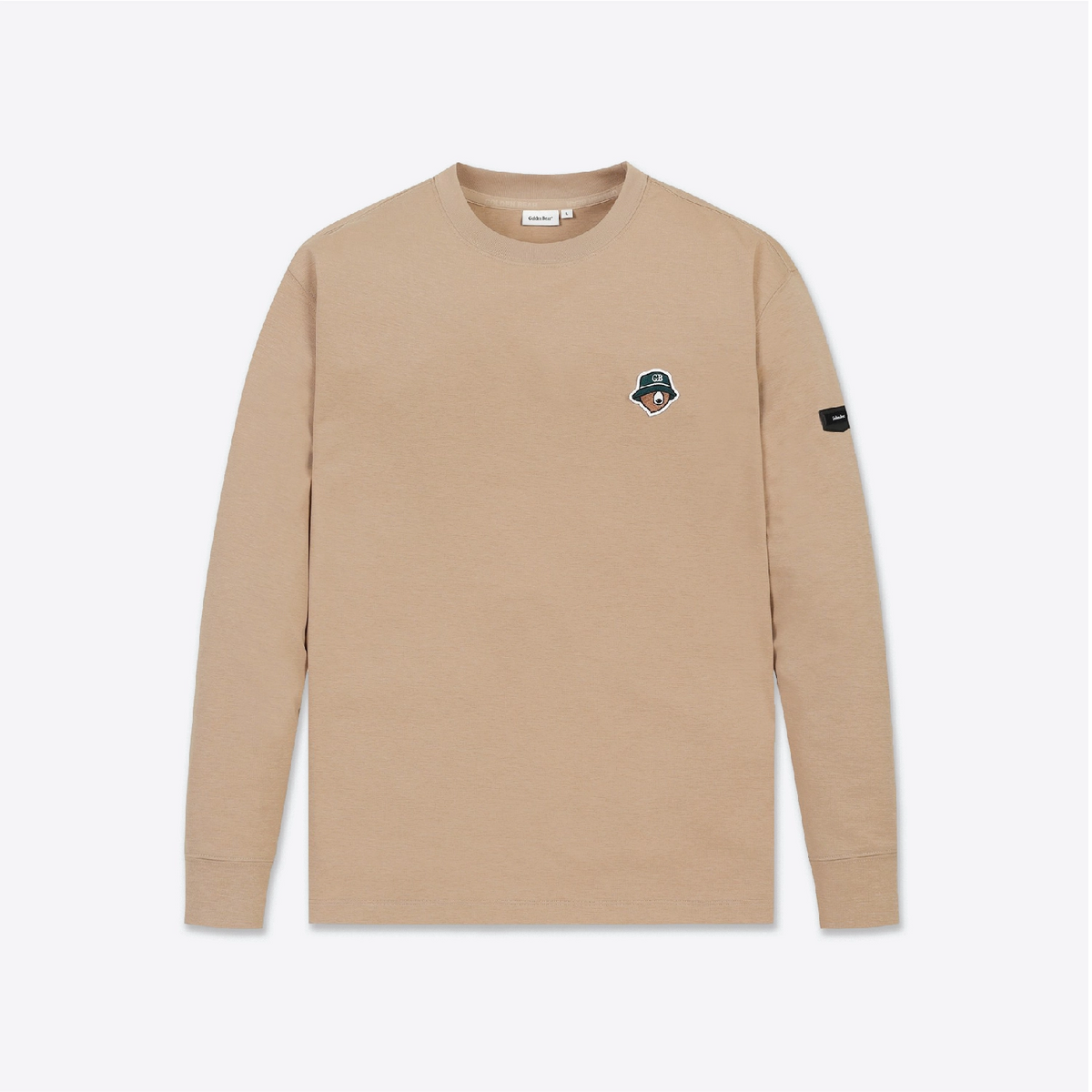 A beige long-sleeve crewneck shirt with a small embroidered patch on the left chest and a black brand patch on the right sleeve, shown against a light gray background.