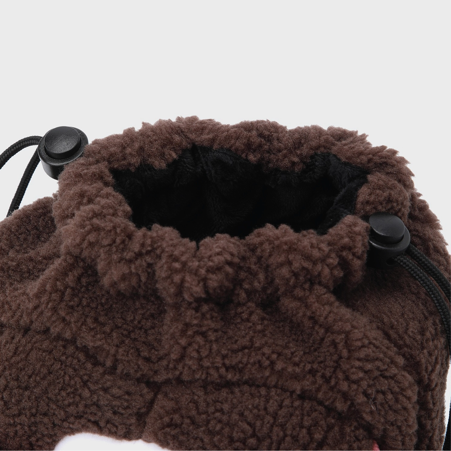 Close-up of a brown sherpa fleece drawstring bag with black drawstring cords and black toggle buttons, set against a plain light gray background.