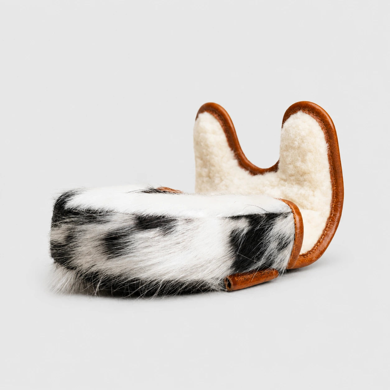 A black and white cow-print faux fur Owaih Center DF3 Putter Cover Black cowhide side view with brown leather trim, featuring a curved U-shaped top edge, shown on a light gray background.