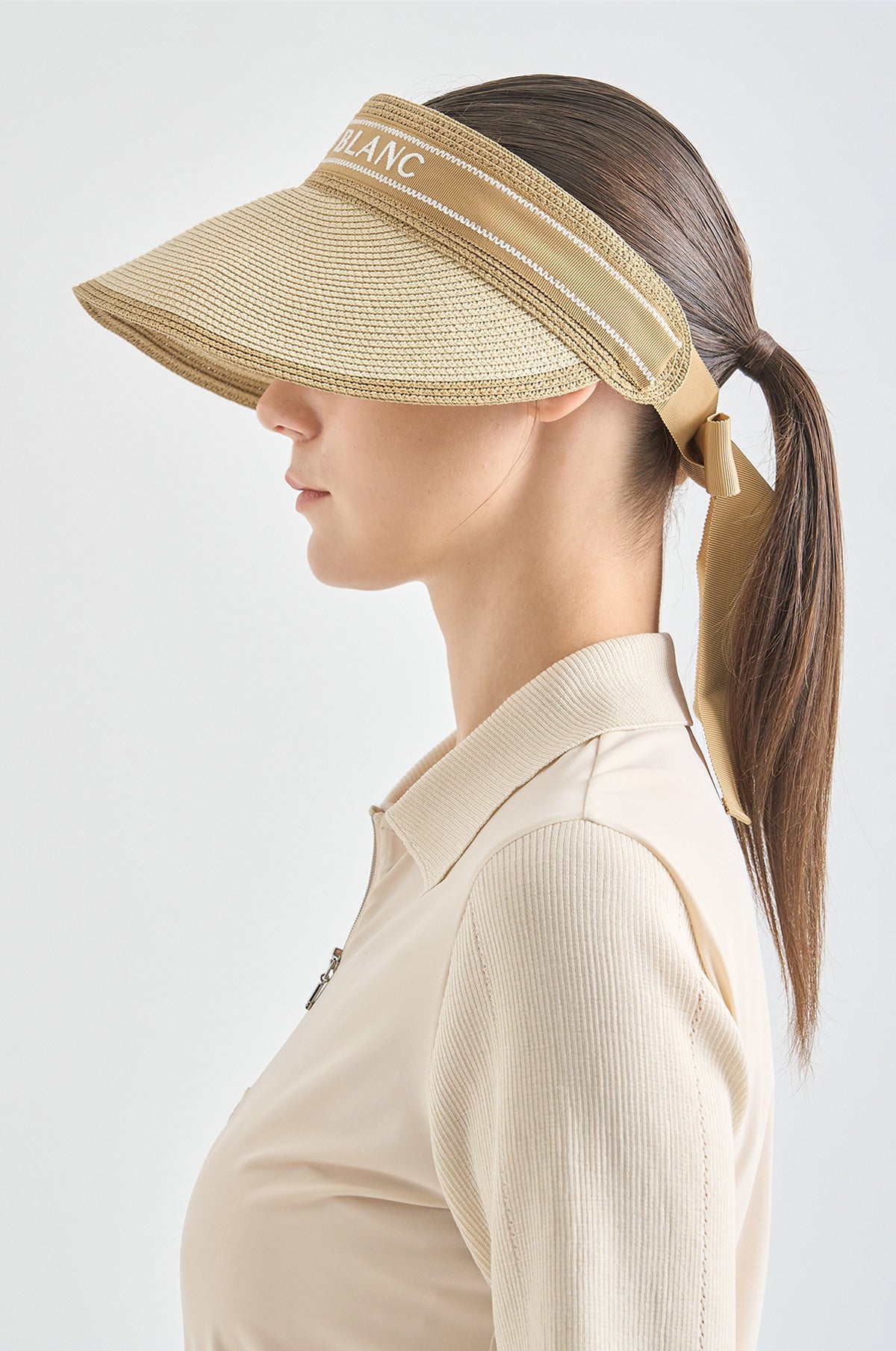 Woman wearing a beige visor and matching shirt on a white background