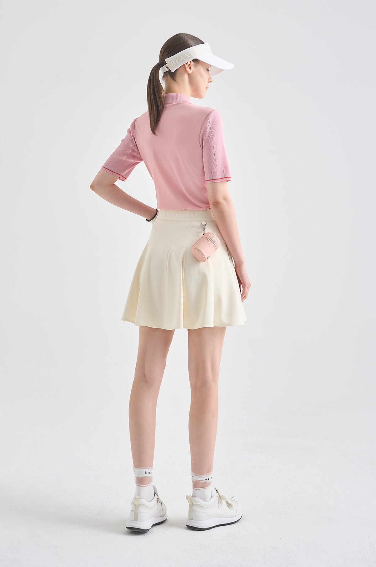 Woman wearing a pink polo shirt, white skirt, and visor on a light gray background