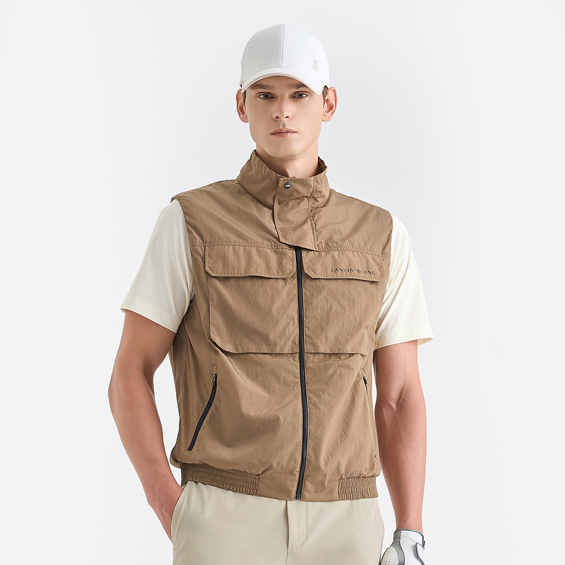 Man wearing a beige vest over a white shirt on a light gray background