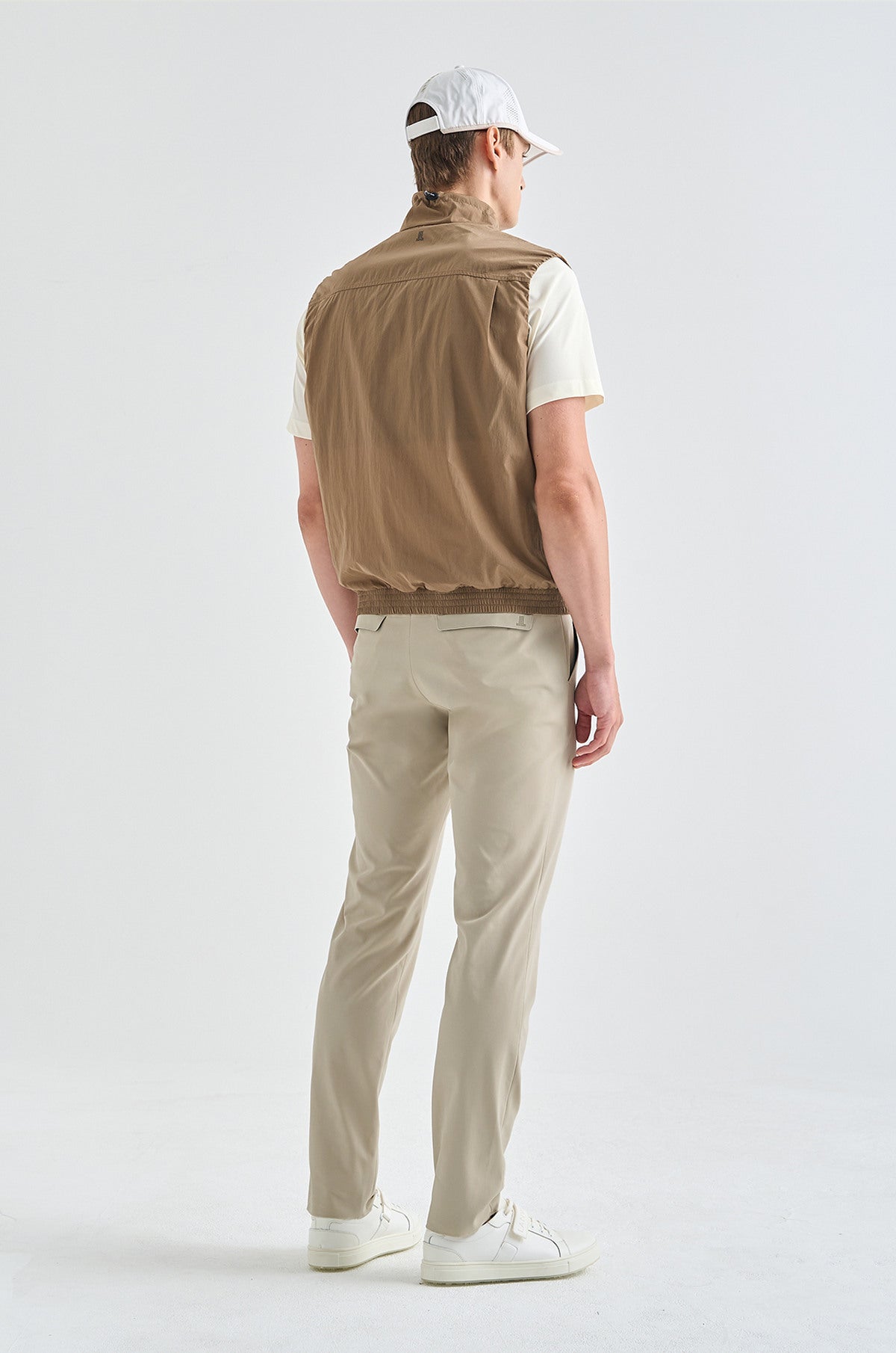 Man wearing a beige vest, white shirt, beige pants, and white cap on a white background