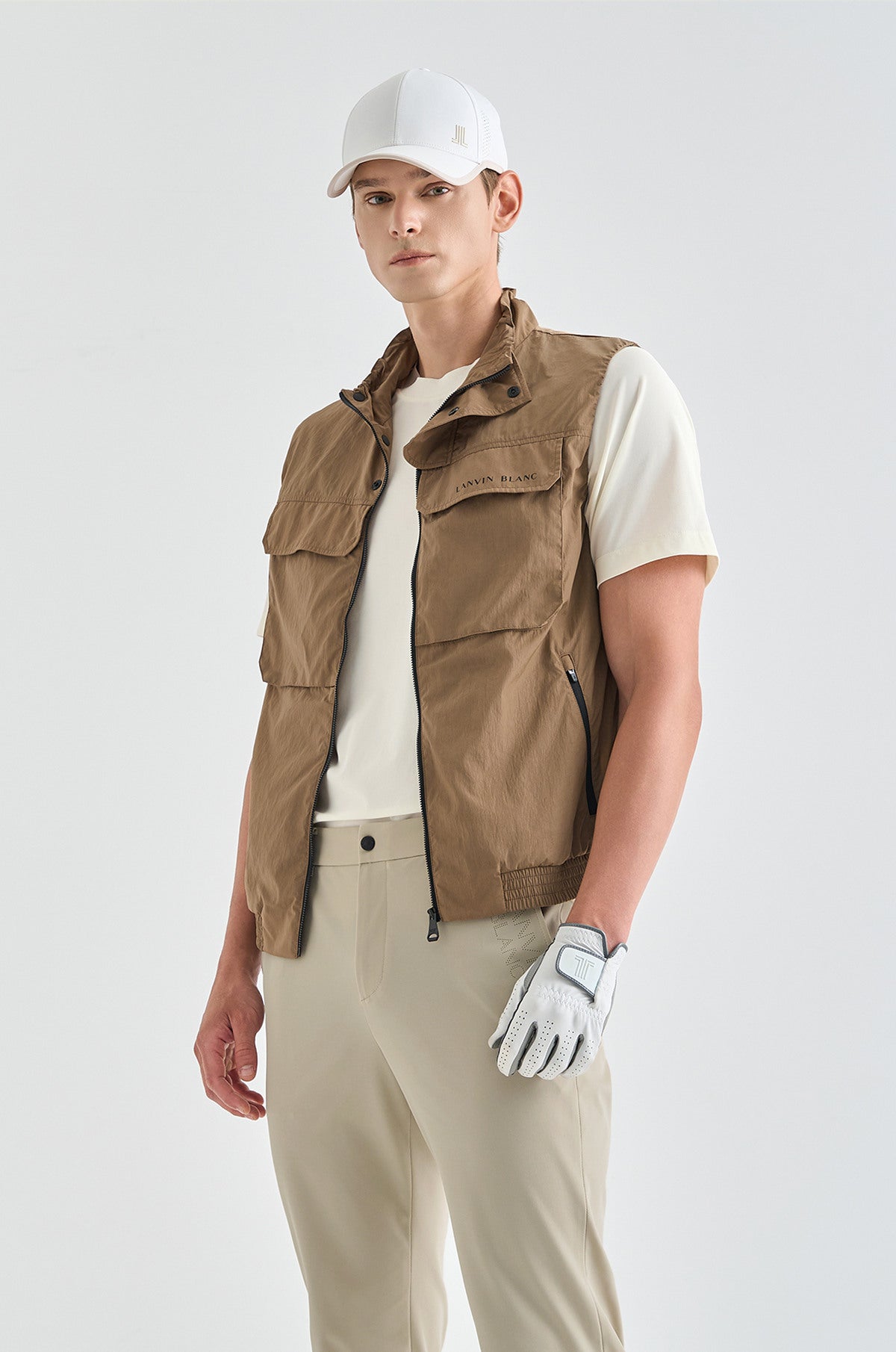 Person wearing a brown vest, white shirt, beige pants, and white cap on a light gray background