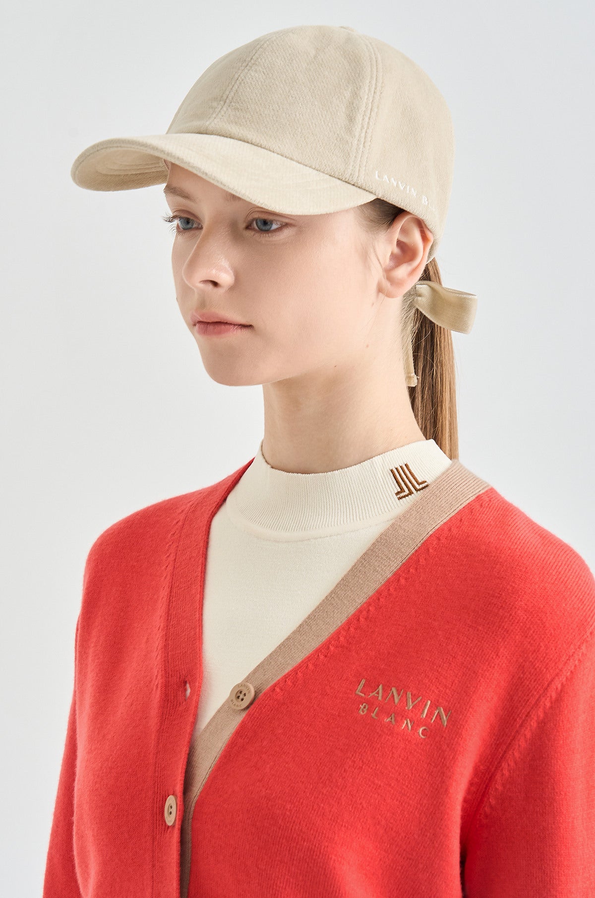 Person wearing a beige cap and red cardigan with a visible brand logo on a light gray background