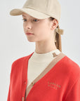Person wearing a beige cap and red cardigan with a visible brand logo on a light gray background
