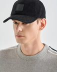 Man wearing a black cap with a small patch on a light gray background