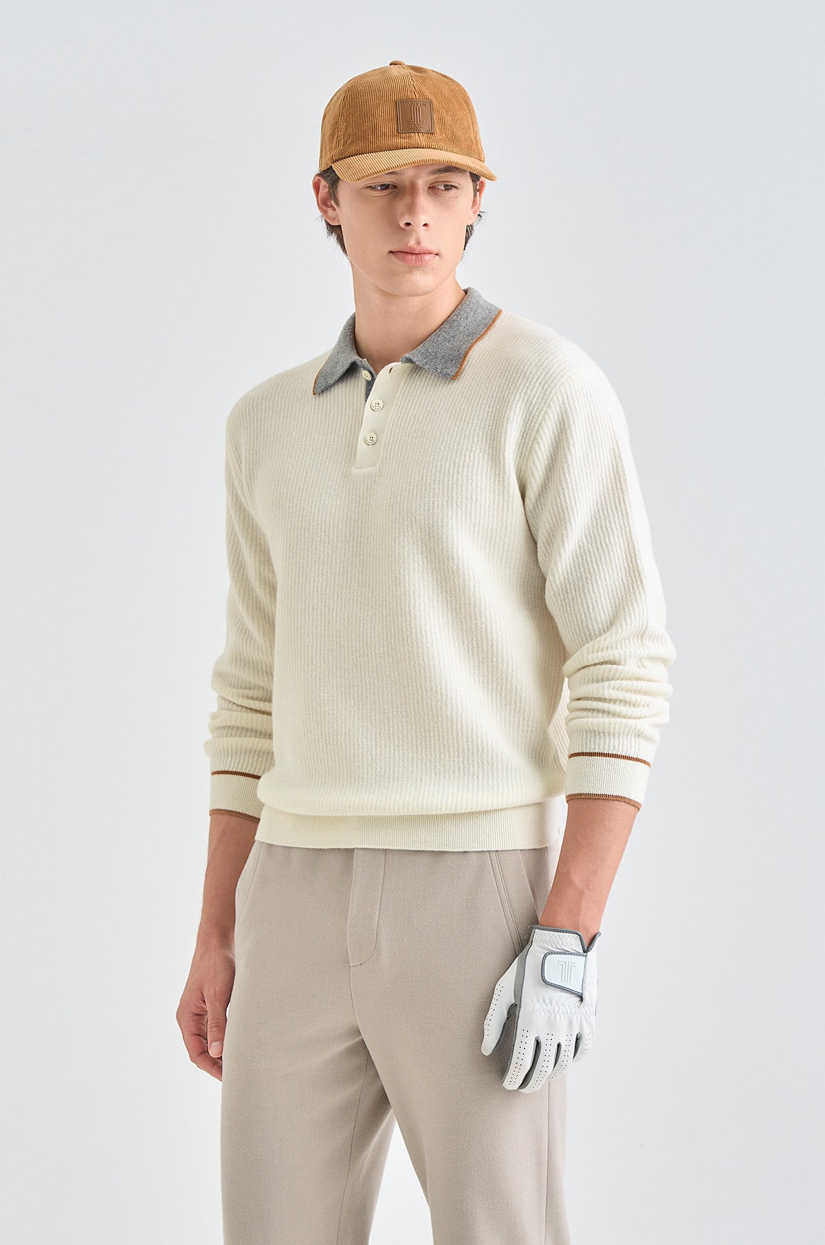 Person wearing a beige sweater, brown cap, and golf glove on a light gray background