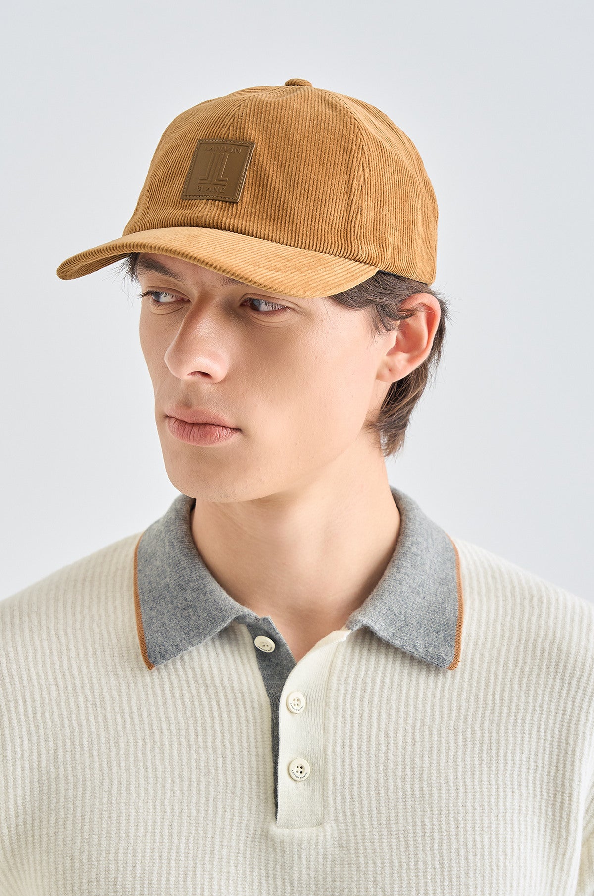 Person wearing a brown cap and light-colored sweater with a gray collar against a white background