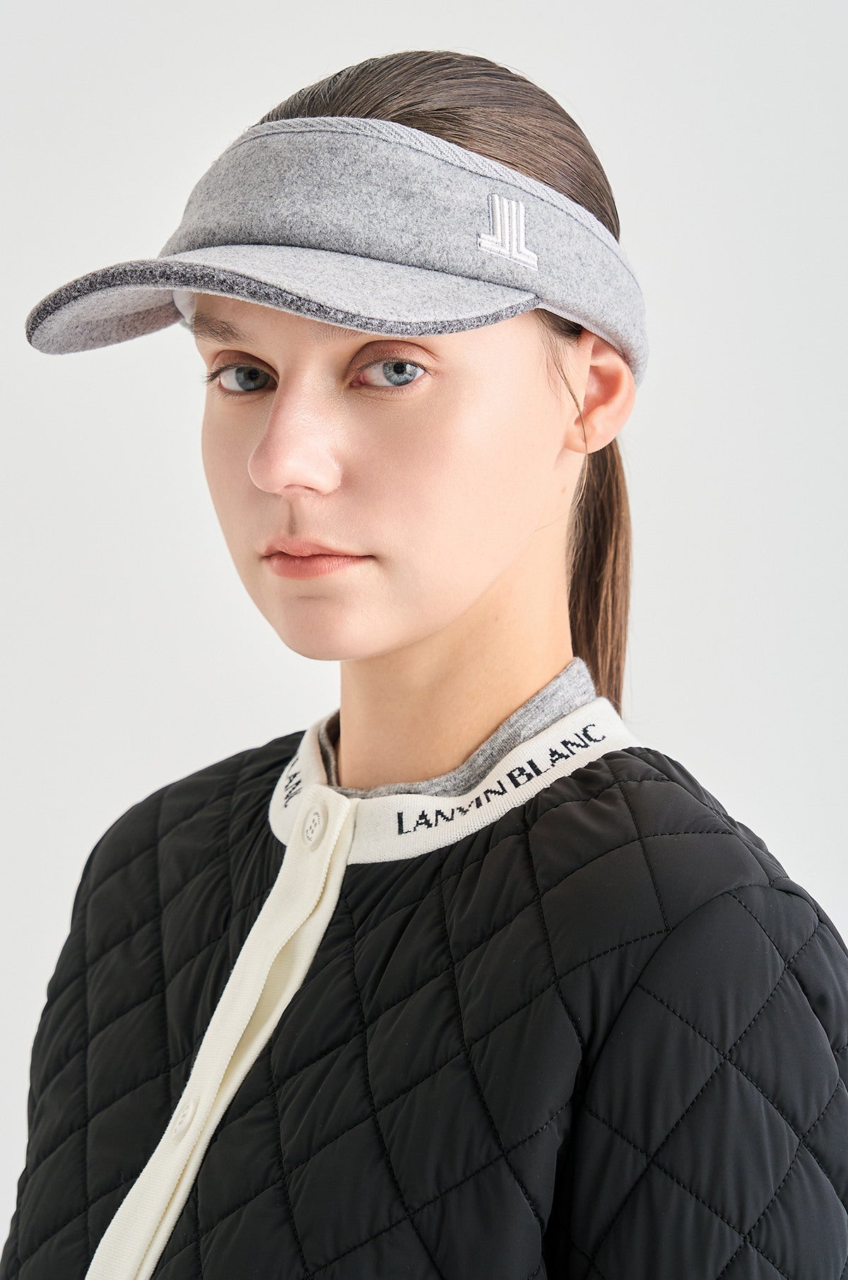Person wearing a gray visor and black quilted jacket with visible branding on a light gray background