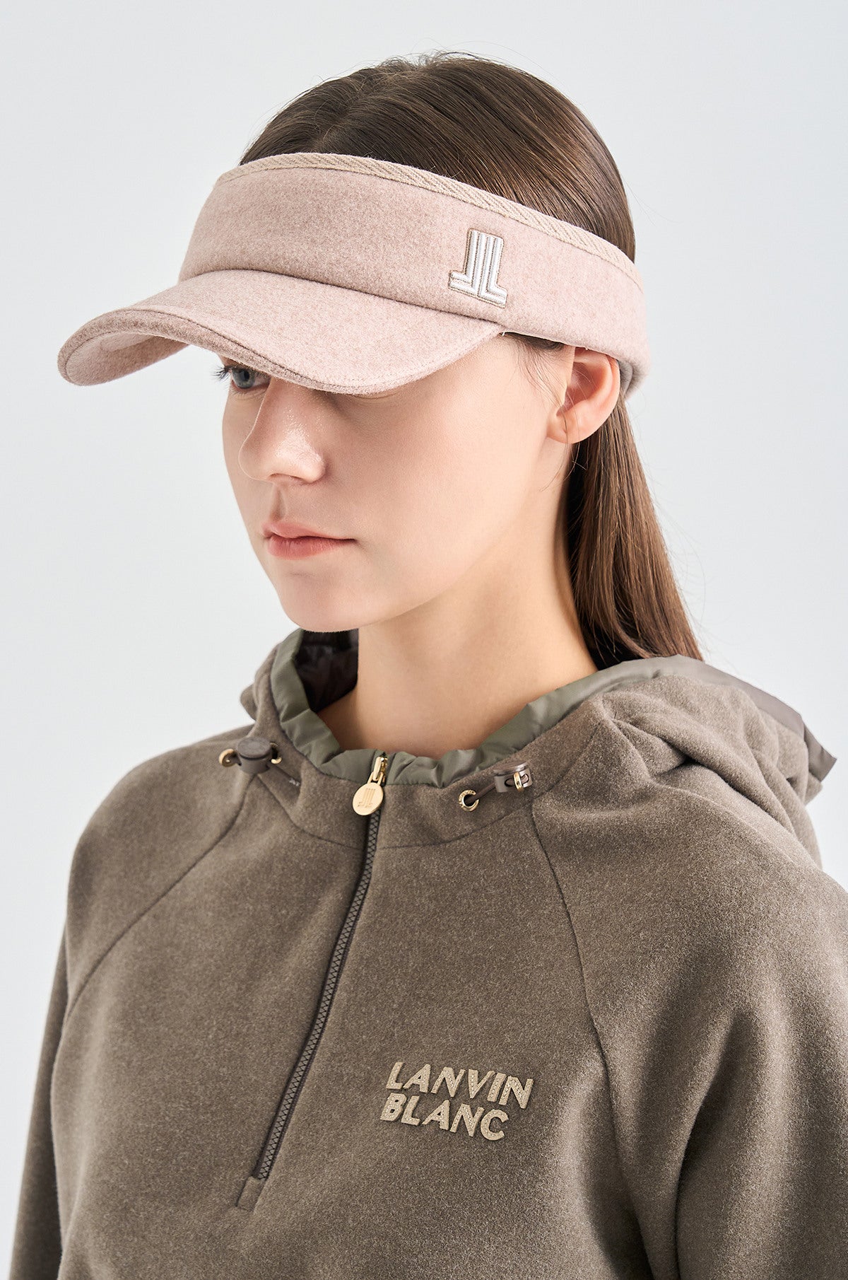 Woman wearing a beige visor and brown hoodie with 'LANVIN BLANC' branding on a light gray background