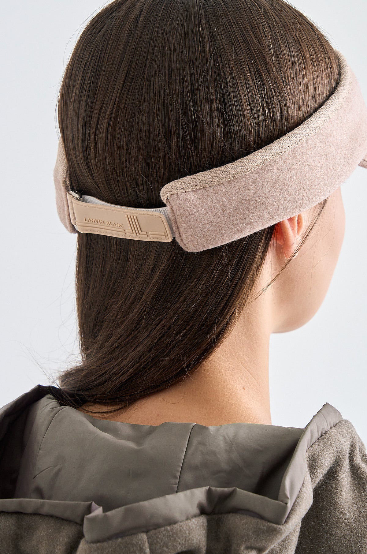 Person wearing a beige headband with a brand logo on a light gray background