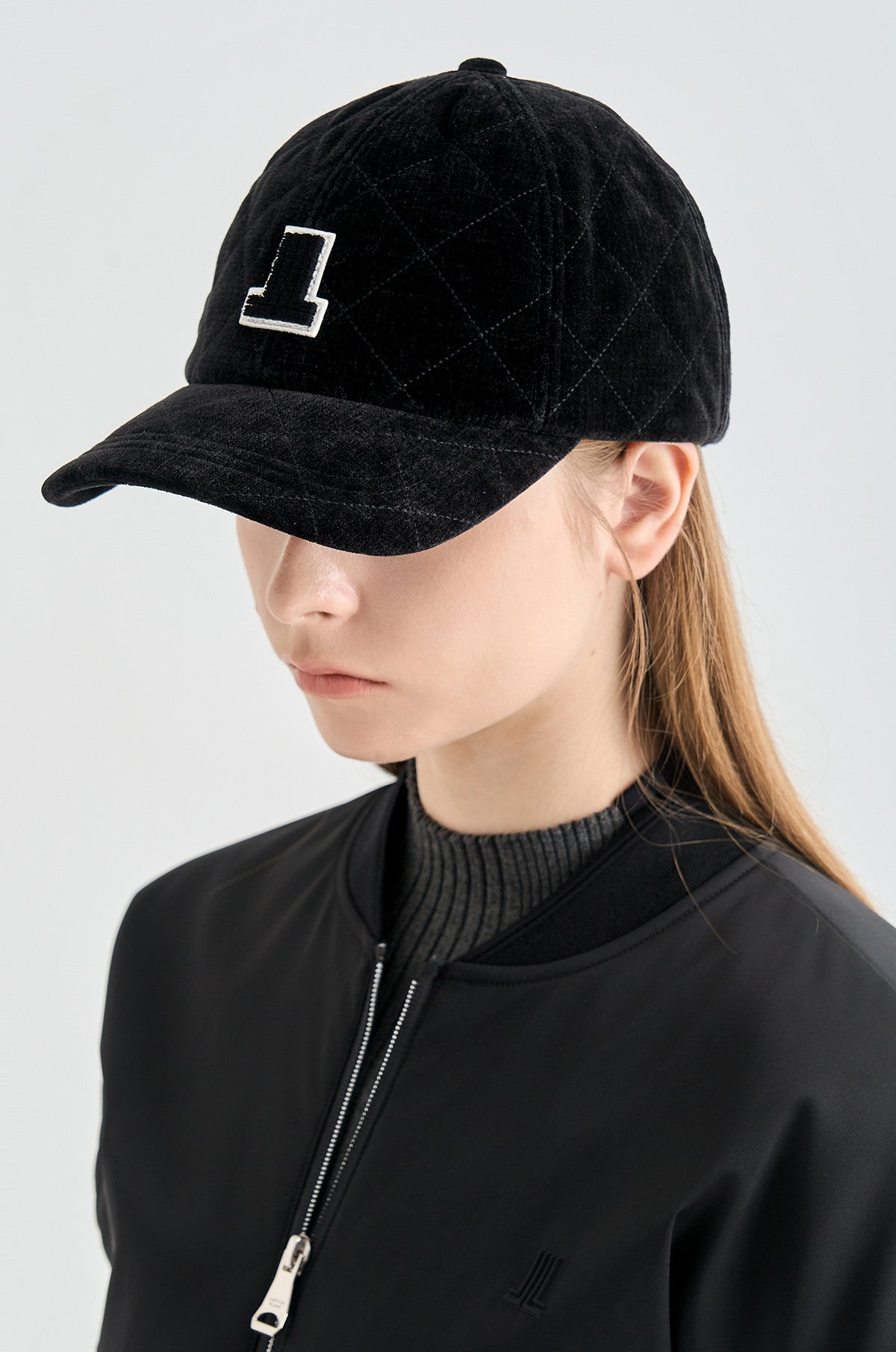Person wearing a black quilted cap with a logo on a light gray background