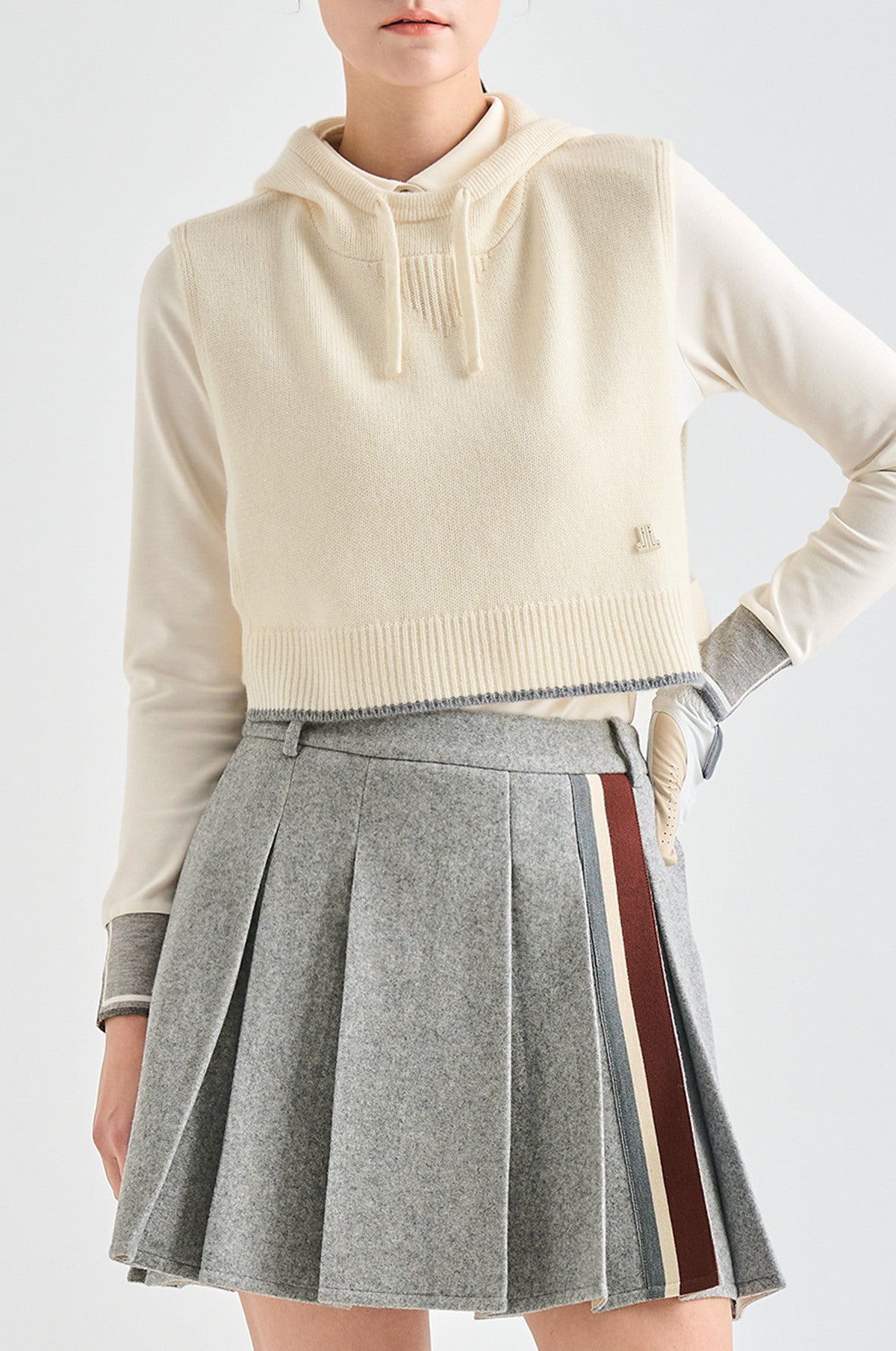 Person wearing a cream hoodie and gray pleated skirt with a stripe on a white background