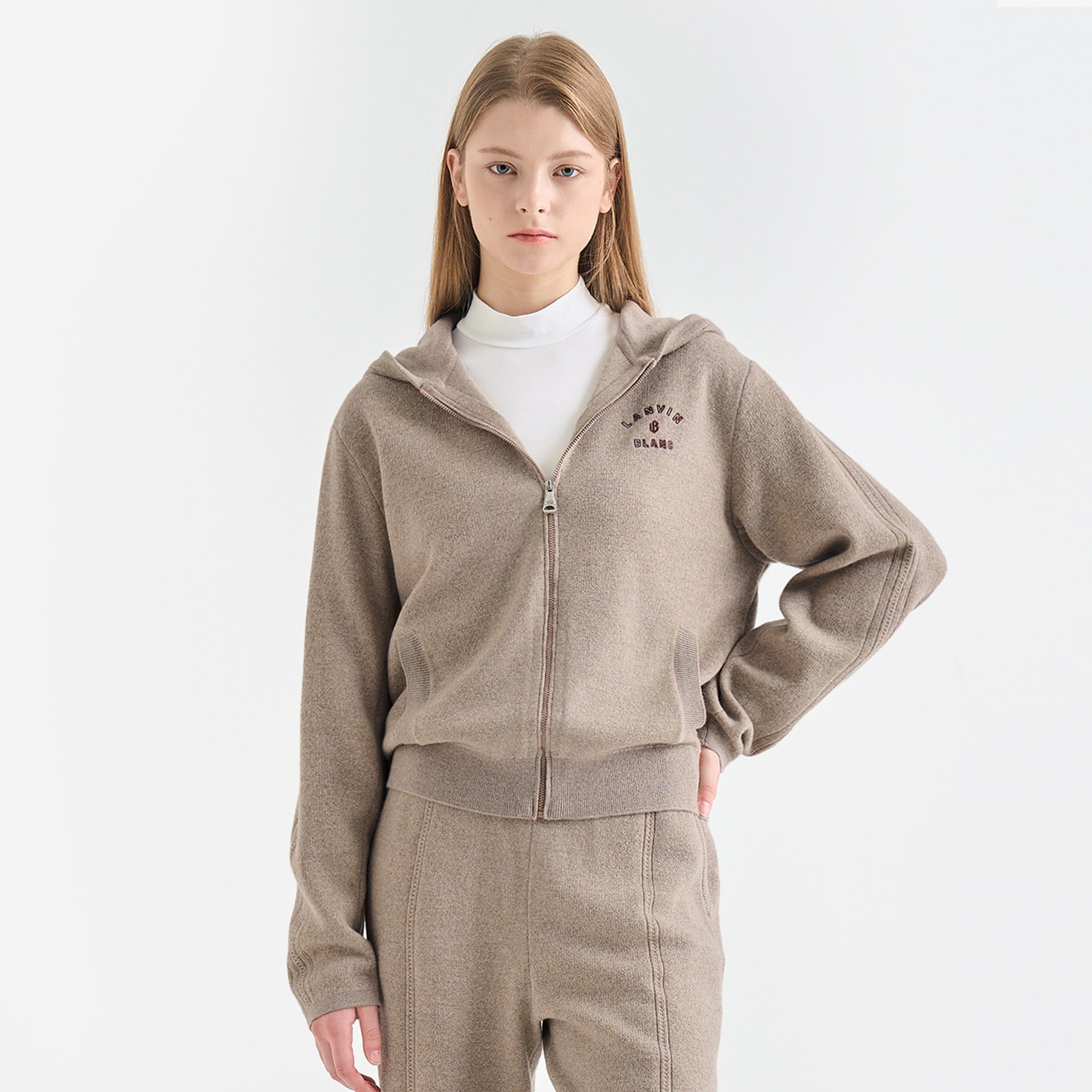 Person wearing a beige hoodie with a brand logo on a white background