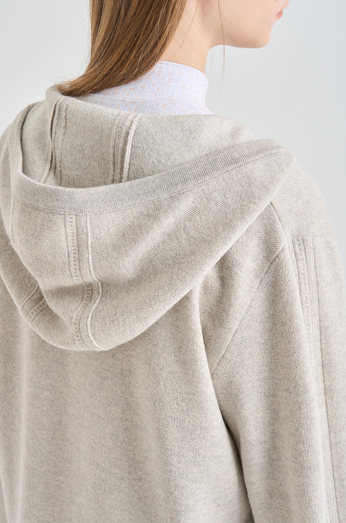 Close-up of a person wearing a beige hoodie with a plain background
