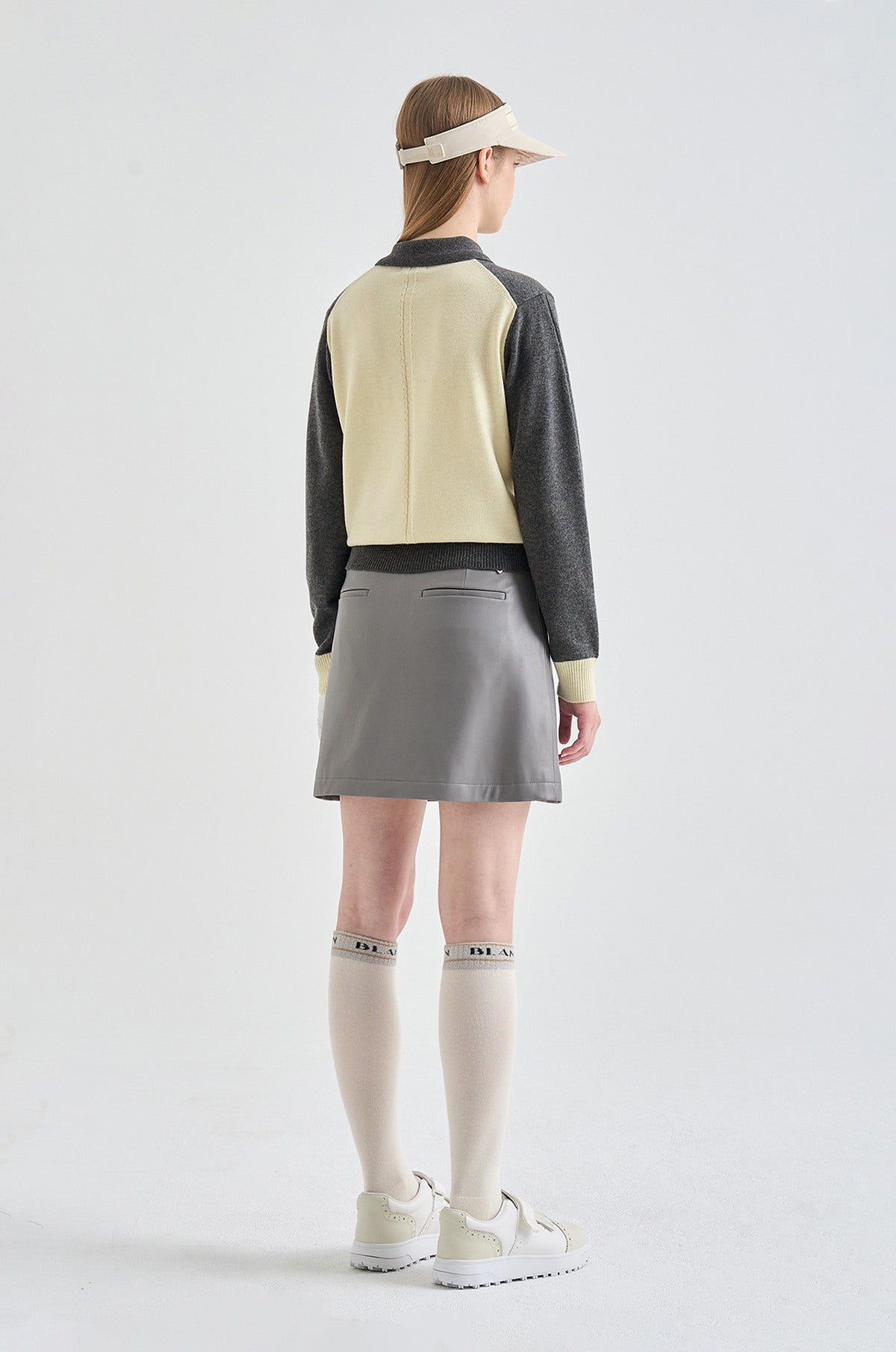 Person wearing a two-tone shirt, gray skirt, and white shoes on a light gray background