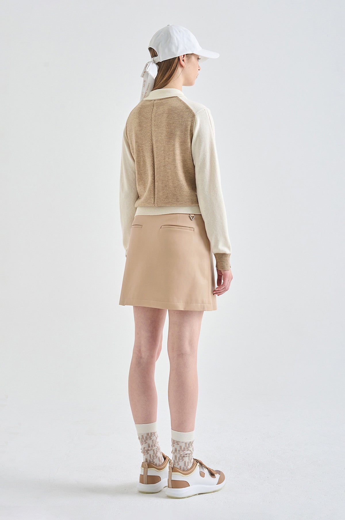Person wearing a beige vest, white shirt, beige skirt, and white cap on a white background