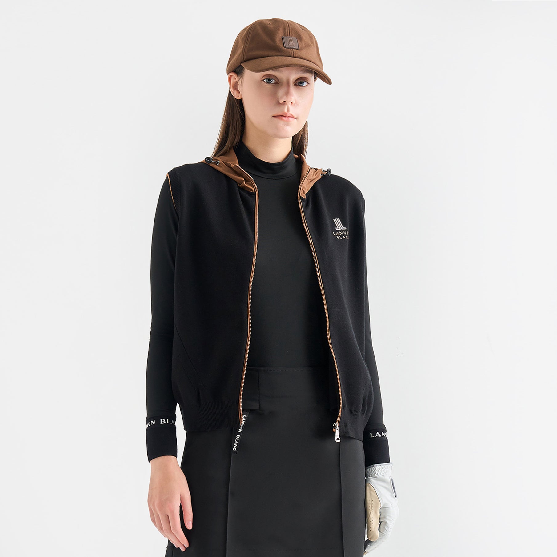 Woman wearing a black jacket with brown accents and a cap on a white background