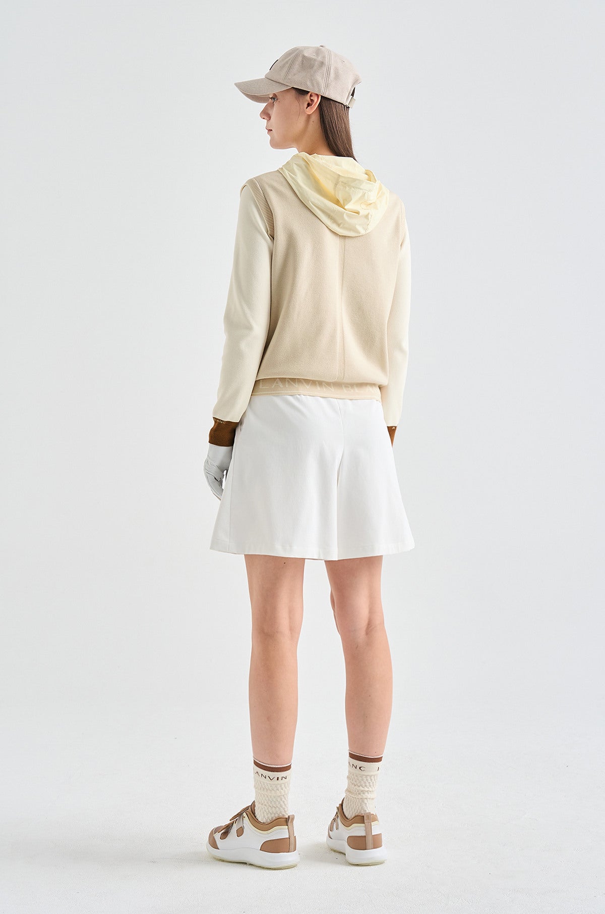 Person wearing a beige hoodie, white skirt, and brown shoes on a white background