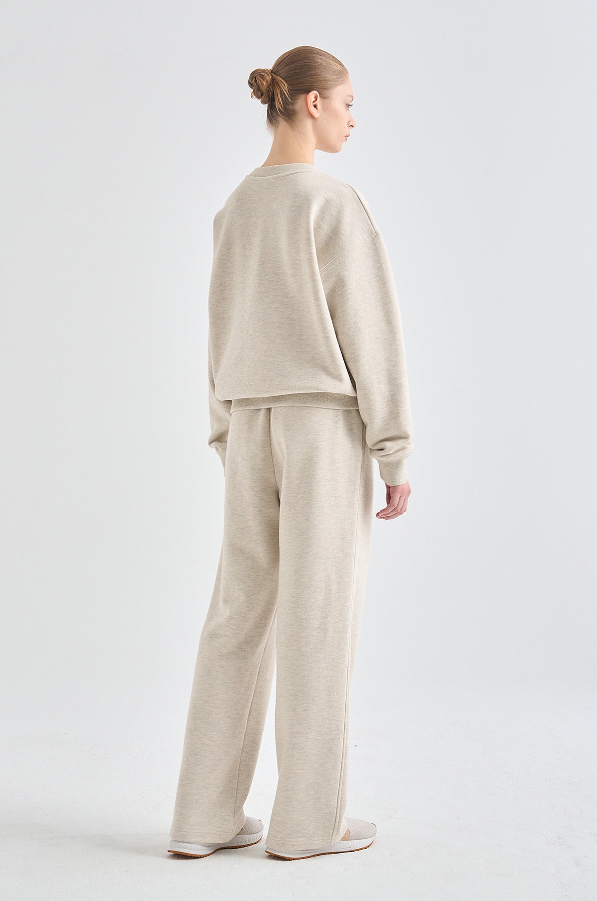 Person wearing a beige sweatshirt and pants set on a white background