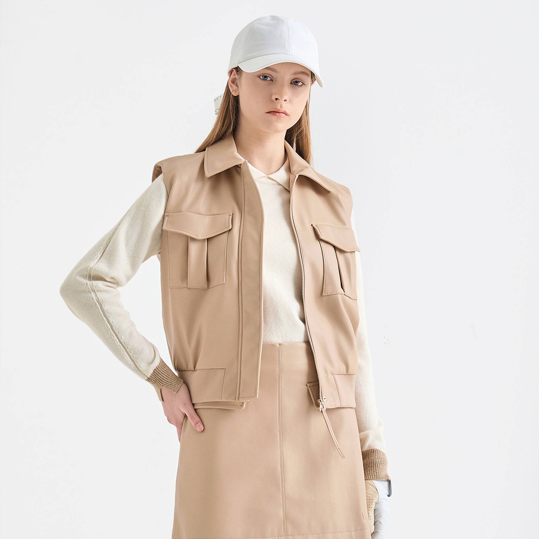 Person wearing a beige jacket over a white shirt with a white cap on a light gray background