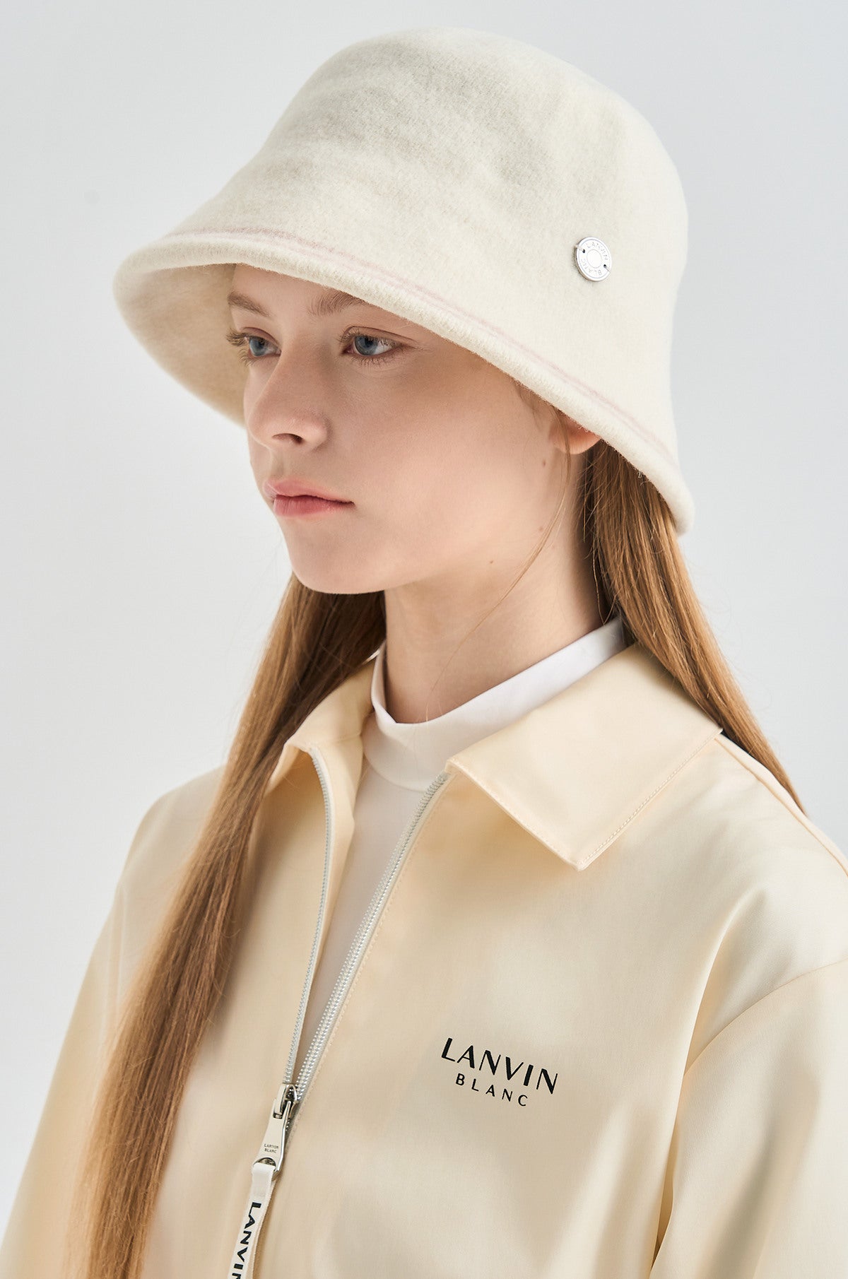Person wearing a cream-colored hat and jacket with 'LANVIN BLANC' branding on a light gray background